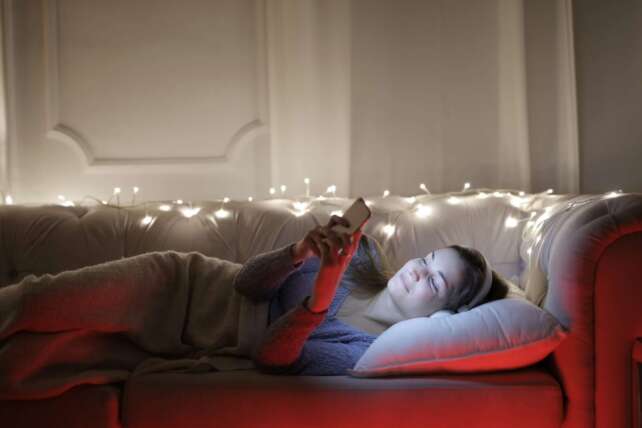 A person relaxed on a sofa in the evening, texting on a phone in warm indoor light