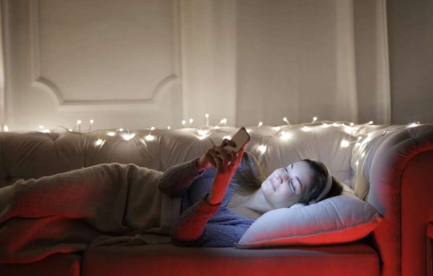 A person relaxed on a sofa in the evening, texting on a phone in warm indoor light
